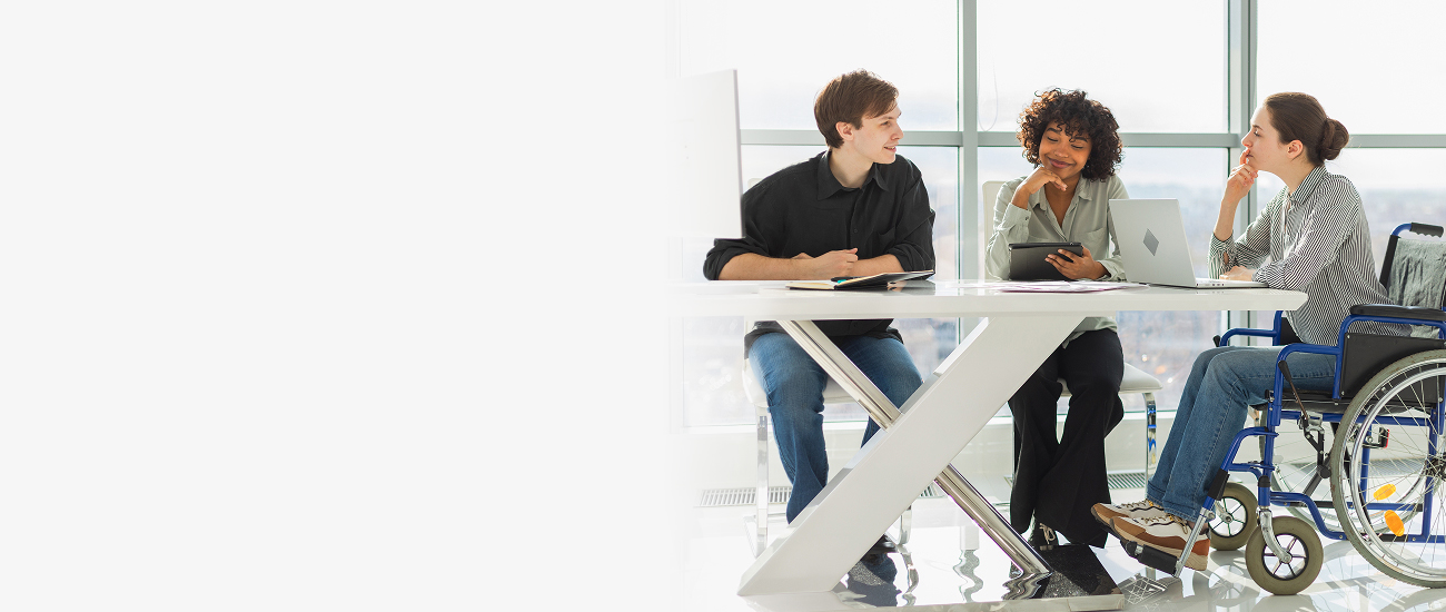 Three colleagues, including a wheelchair user, collaborating around a table in a bright, modern office.